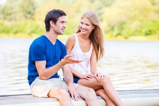 Having a great date. Beautiful young loving couple sitting at the quayside together and smiling