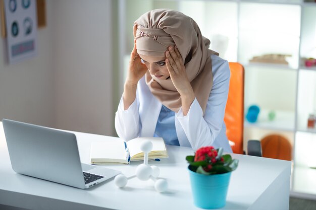 Avere mal di testa. scienziato medico che indossa l'hijab ha mal di testa dopo aver lavorato tutto il giorno