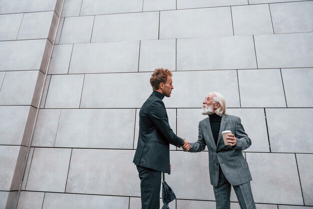 Photo having a meet young guy with senior man in elegant clothes is outdoors together conception of business