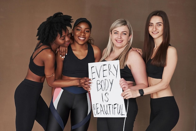 Photo having nice time group of multi ethnic women standing in the studio against brown background