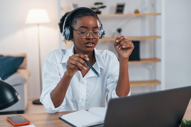 Having online meeting Young african american woman in white shirt is at home