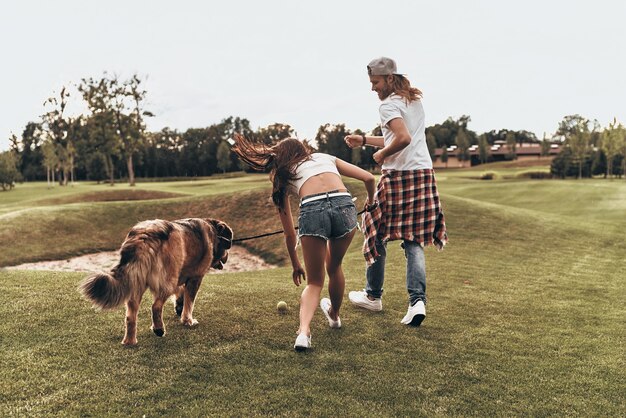 Photo having so much fun together.  full length rear view of young modern couple playing with their dog while walking in the park