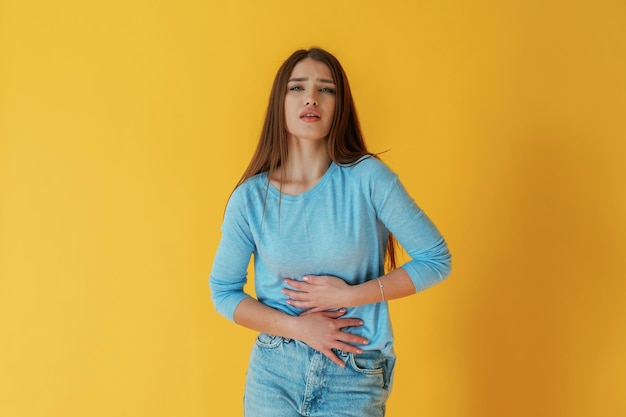 Having stomach pain Young woman is against yellow background