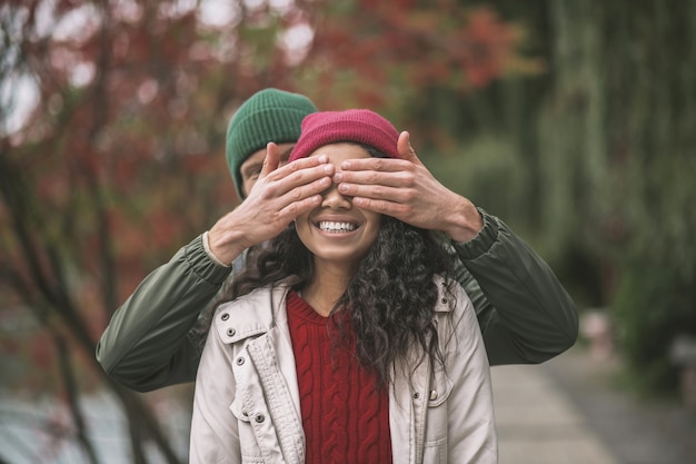 Having a surprise. A man closing womans eyes while walking together