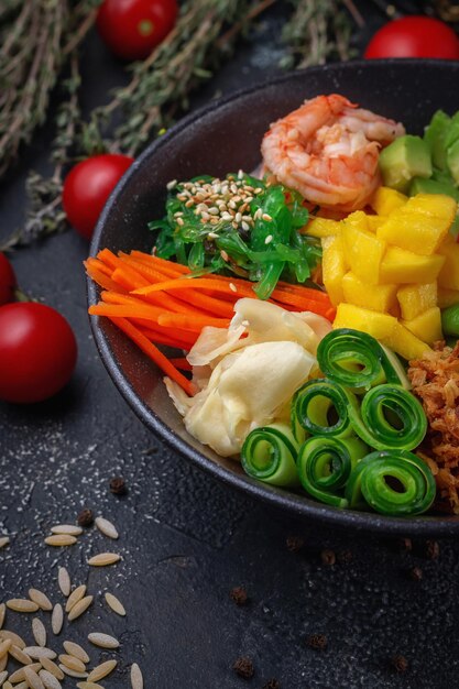 Hawaii garnalen poke met groenten met gember, mango, komkommer en avocado, rijst, zeewier, tomaat. aziatische zalmpor op donkere steenachtergrond.