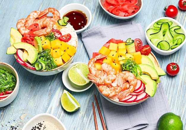 Hawaii shrimp poke avocado mango rice seaweed cucumber radish\
in bowl home made vegetarian prawn poke seafood concept asian\
shrimp poke salad on blue wood background