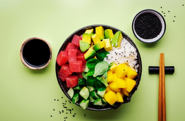 Hawaiiaanse poke bowl met tonijn avocado mango komkommer veldsla en witte rijst Sojasaus limoen en sesam dressing Groene tafel achtergrond bovenaanzicht