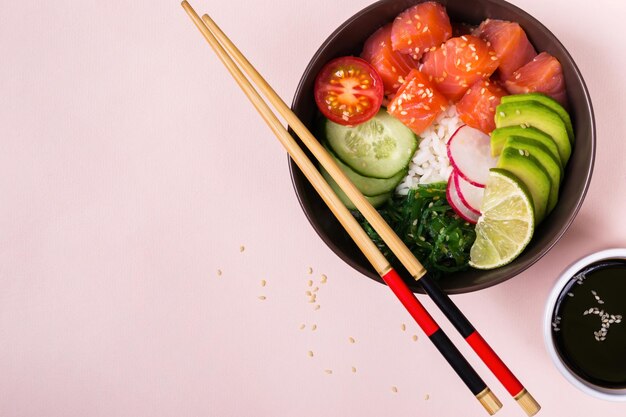 Hawaiiaanse zalmzaksalade met rijst, groenten en zeewier op roze achtergrond.