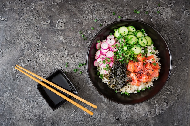 Hawaiian fish poke bowl with rice, radish, cucumber, tomato, sesame seeds and seaweeds. 