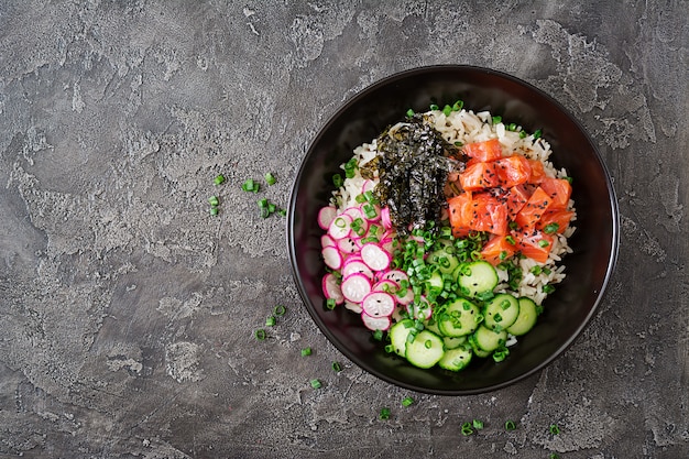 Hawaiian fish poke bowl with rice, radish, cucumber, tomato, sesame seeds and seaweeds. 