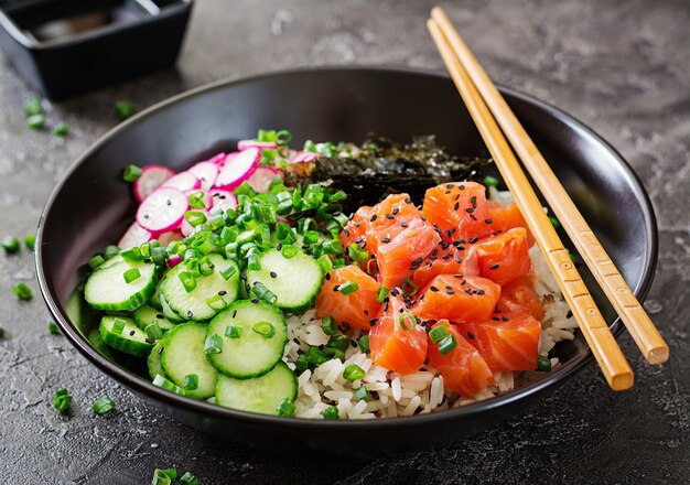 Hawaiian fish poke bowl with rice, radish, cucumber, tomato, sesame seeds and seaweeds. 