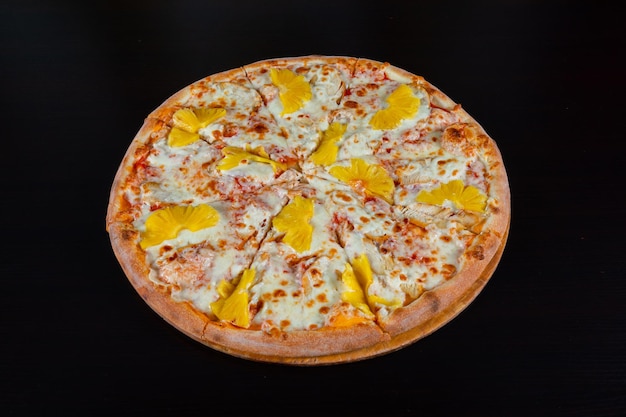 Hawaiian pizza topped with pineapple on a black background