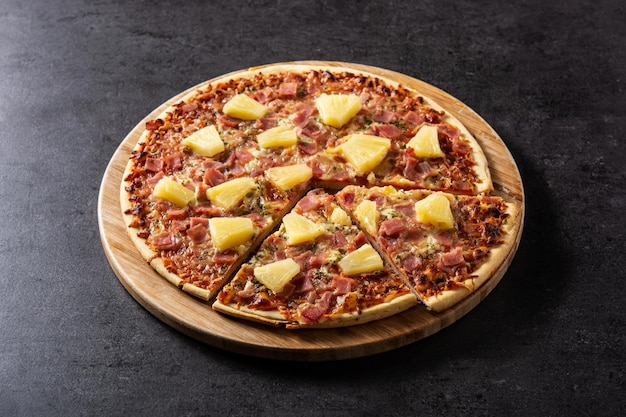 Hawaiian pizza with pineappleham and cheese on black slate background