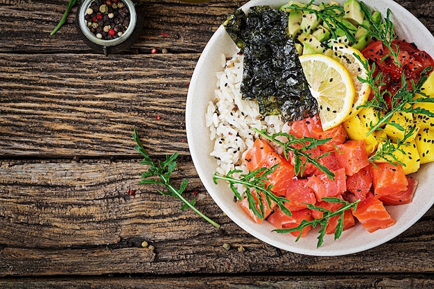 Hawaiian salmon fish poke bowl with rice, avocado, mango, tomato, sesame seeds and seaweeds.