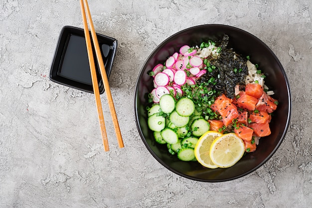 Hawaiian salmon poke bowl with rice, radish,cucumber, tomato, sesame seeds and seaweeds