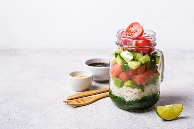 Hawaiian salmon poke salad in glass jar with rice and vegetables, selective focus.