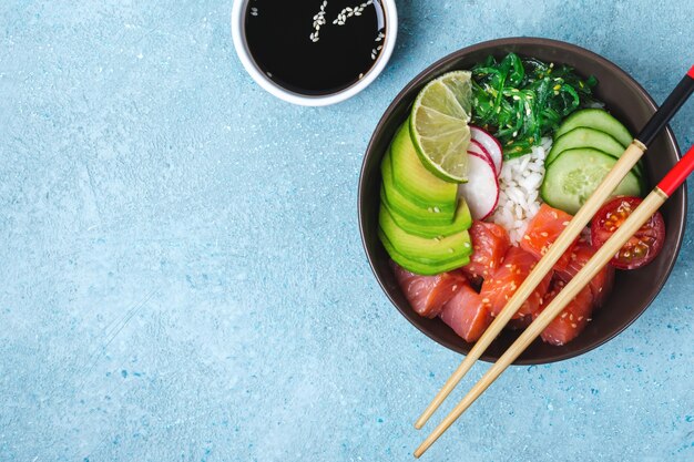 Hawaiian salmon poke salad with rice, vegetables and seaweed on blue background.