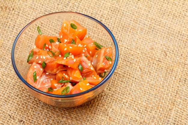 Hawaiian salmon poke with green onions and sesame seeds in glass bowl with copy space. Organic seafood