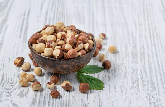 Hazelnoten rauw en gepeld in een houten beker op een witte houten achtergrond Rustieke stijl Het concept van vegetarische en dieetsnacks