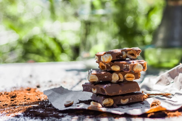 Hazelnut and almond milk chocolate pieces tower on a wooden table with nature blurred background