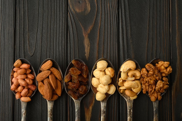 Hazelnut cashews raisins almonds peanuts walnuts in silver spoons on a rustic background