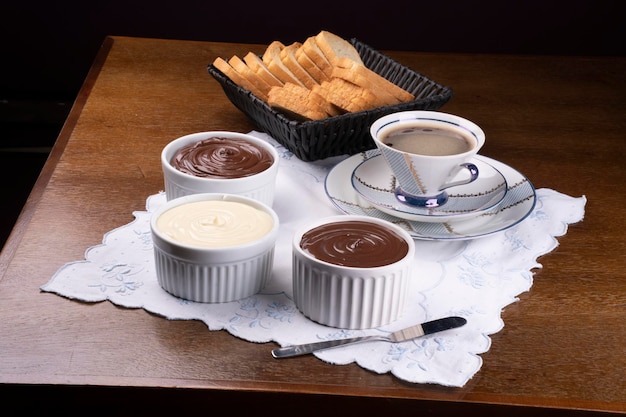 Foto creme al cioccolato alla nocciola e cioccolato bianco con cialde sul tavolo della tazza della colazione del caffè e vista angolare del cestino del pane