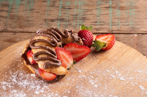 Hazelnut cream croissant dessert with strawberry on wooden board on rustic table closeup