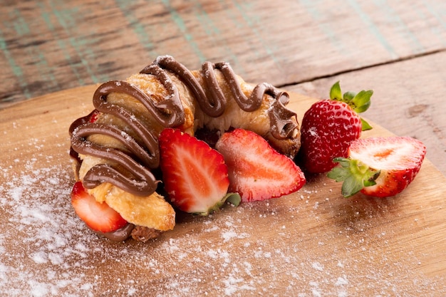 Hazelnut cream croissant dessert with strawberry on wooden board on rustic table in corner in bistro closeup