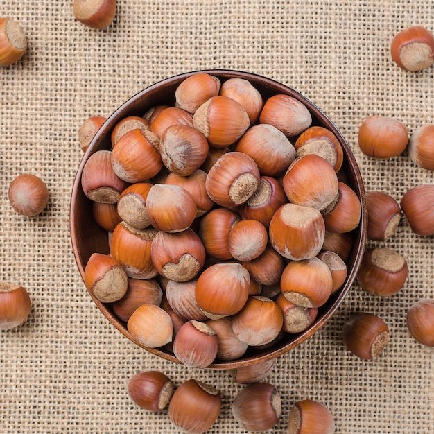 Hazelnut in peel on a light burlap in a wooden bowl.