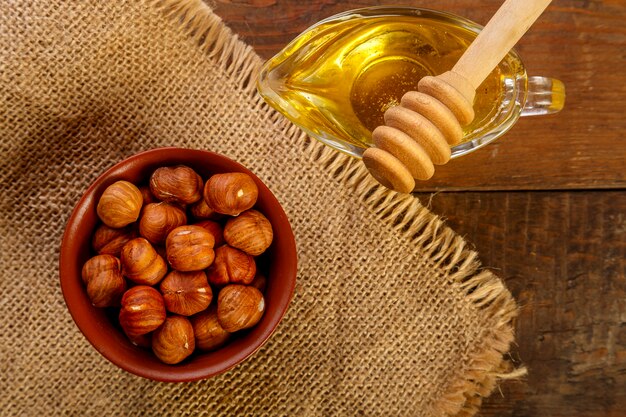 Hazelnuts in a bowl on a sacking next to honey with a spoon on a wooden table Horizontal photo