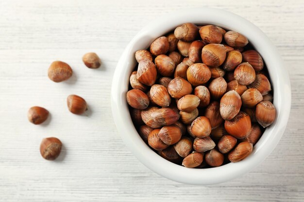Hazelnuts in the bowl on white wooden background
