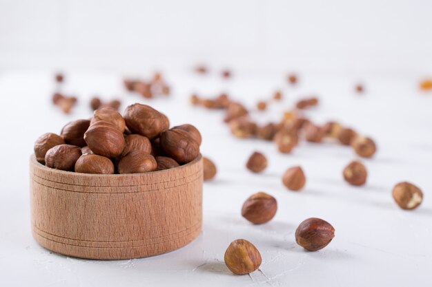 Hazelnuts in brown wooden bowl on white background