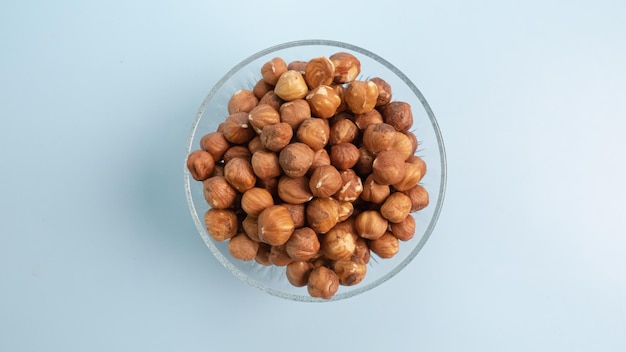 Hazelnuts in transparent glass bowl top view isolated on blue background Concept of healthy oils