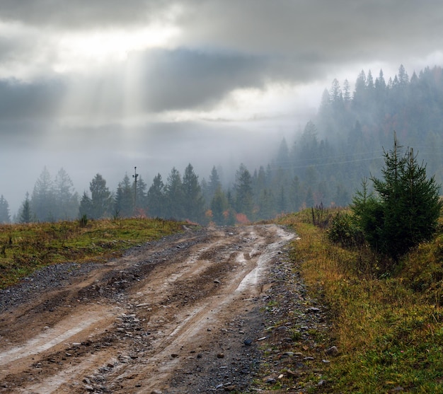秋のカルパティア山脈と汚れた田舎道ウクライナのもやと曇りの早朝