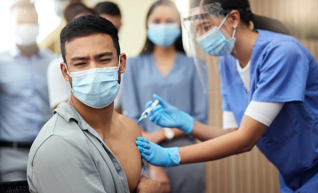 He doesnt like needles Cropped shot of a handsome young businessman getting his covid vaccination from a female nurse in the office