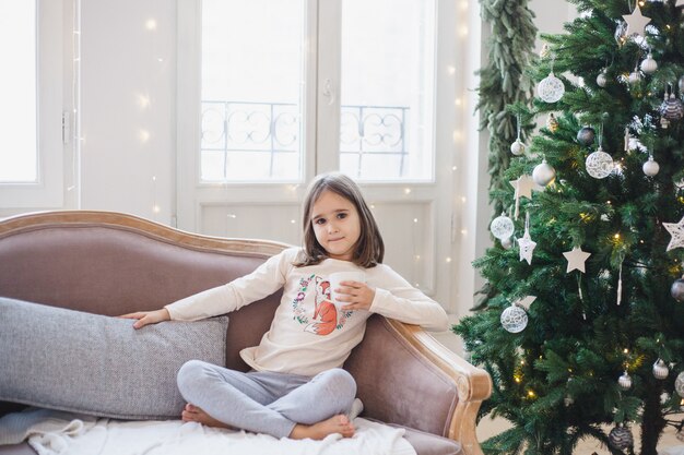 he girl is sitting on the couch waiting for the holiday, the room is decorated for Christmas