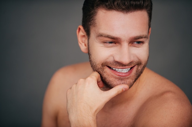 He got candid smile. Confident young shirtless man holding hand on chin and smiling