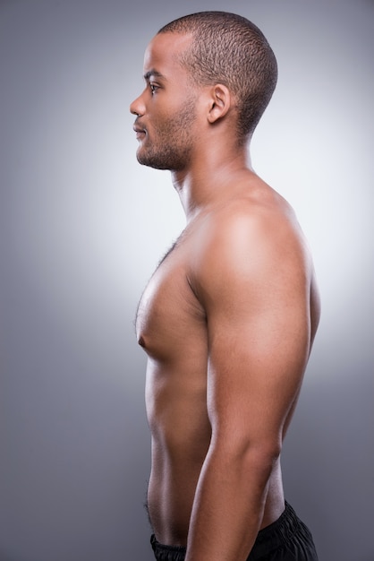 He got perfect body. Side view of young shirtless African man standing against grey background