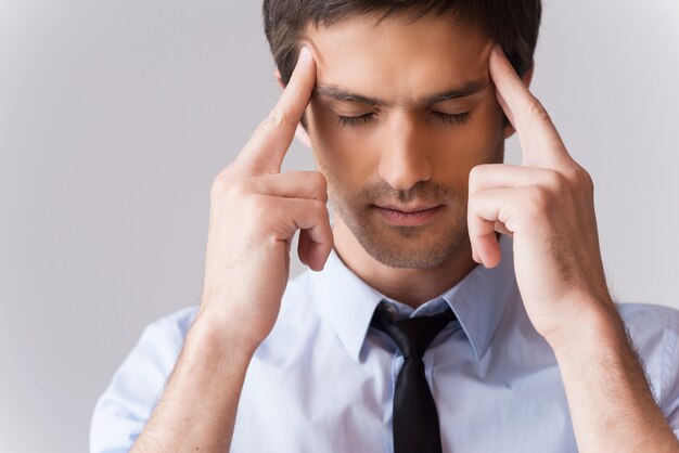 He got stressful job. Young man in shirt and tie touching head with fingers and keeping eyes closed