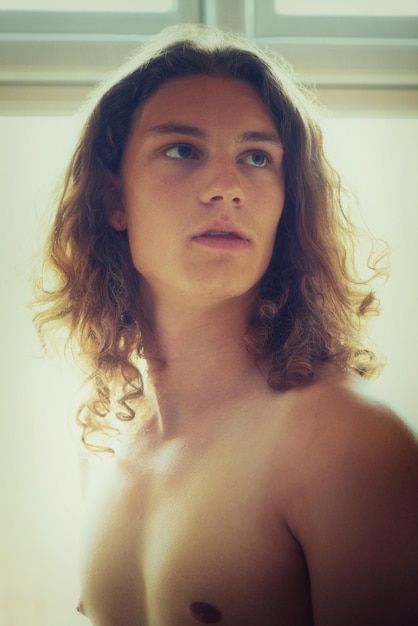 He has an intense stare A young handsome shirtless man standing next to a window