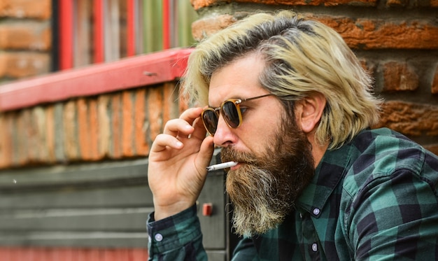 Photo he is serious. brutal mature hipster smoking cigarette. bad habits concept. harmful for your health. smoke nicotine addicted. he is heavy smoker. bearded man in glasses relax with cigarette.