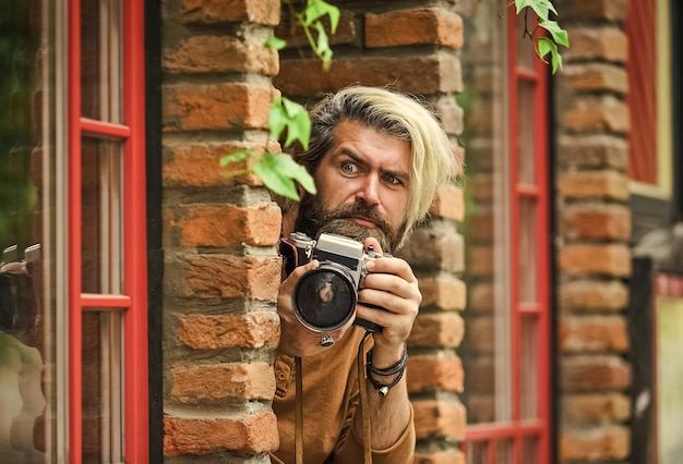 He is spy professional photographer use vintage camera bearded man hipster take photo photo shooting outdoor brutal man traveler with retro camera photography in modern life travel tips