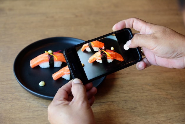 He is using a cellphone, taking a picture of sushi, placed in front of a Japanese restaurant.