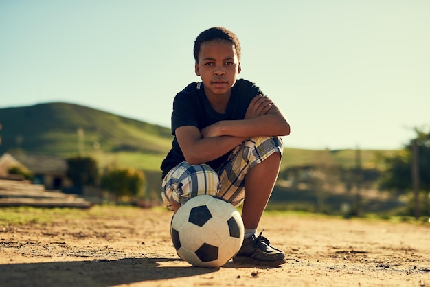 He loves the beautiful game Portrait of a little boy crouching on a field outside with a soccer ball