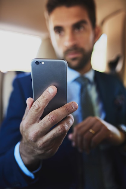 He needs his mobile phone on him at all times Shot of a focused young businessman holding his cellphone while being seated in the back off a car