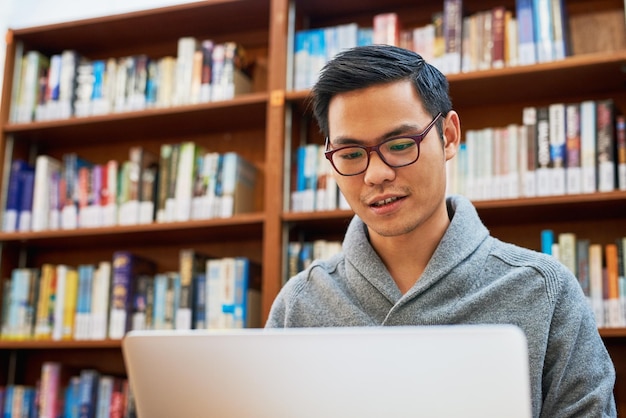 He only strives for success through hard work Shot of a focused young man busy working on his laptop and studying while being seated inside of a library