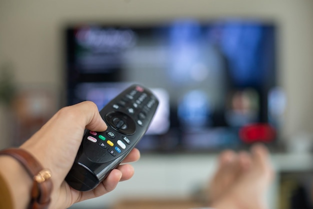 He's sitting on the sofa in the living room and holding a remote.