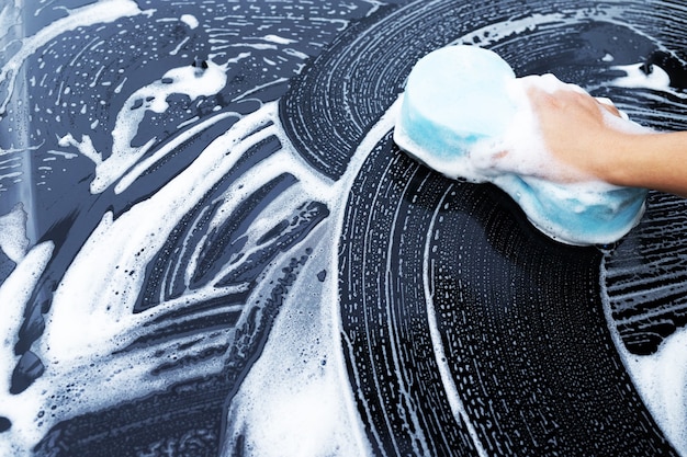 彼は車を洗うために青いスポンジと泡で車を洗っていました。