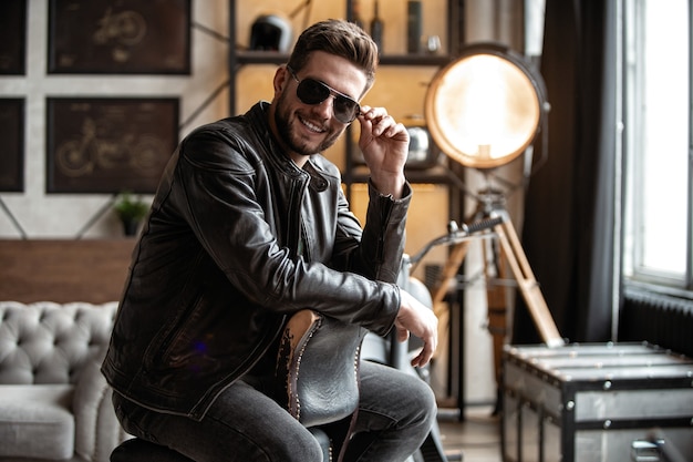 He will melt your heart. Handsome young man in leather jacket looking away while sitting on the stool
