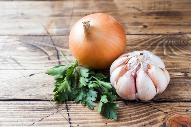 Head of garlic, onion and parsley on wooden table.